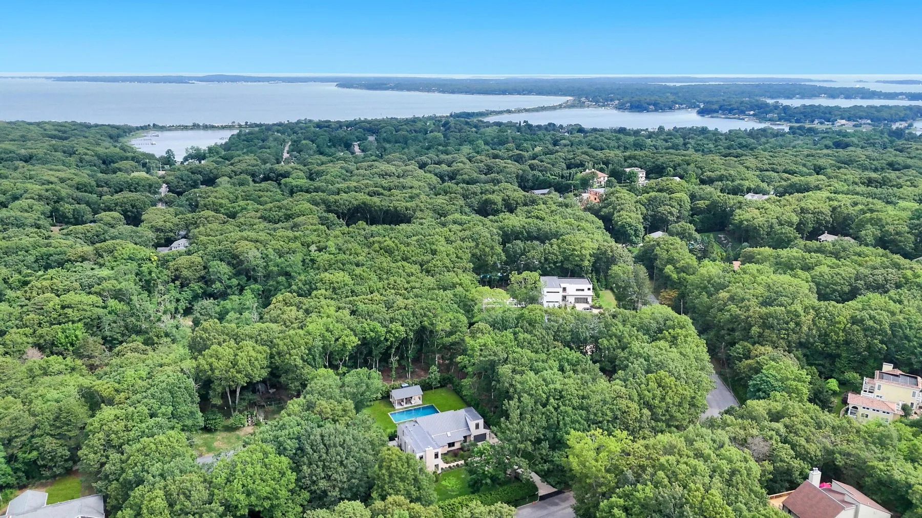 An aerial view of a wooded area with scattered houses and water in the distance.