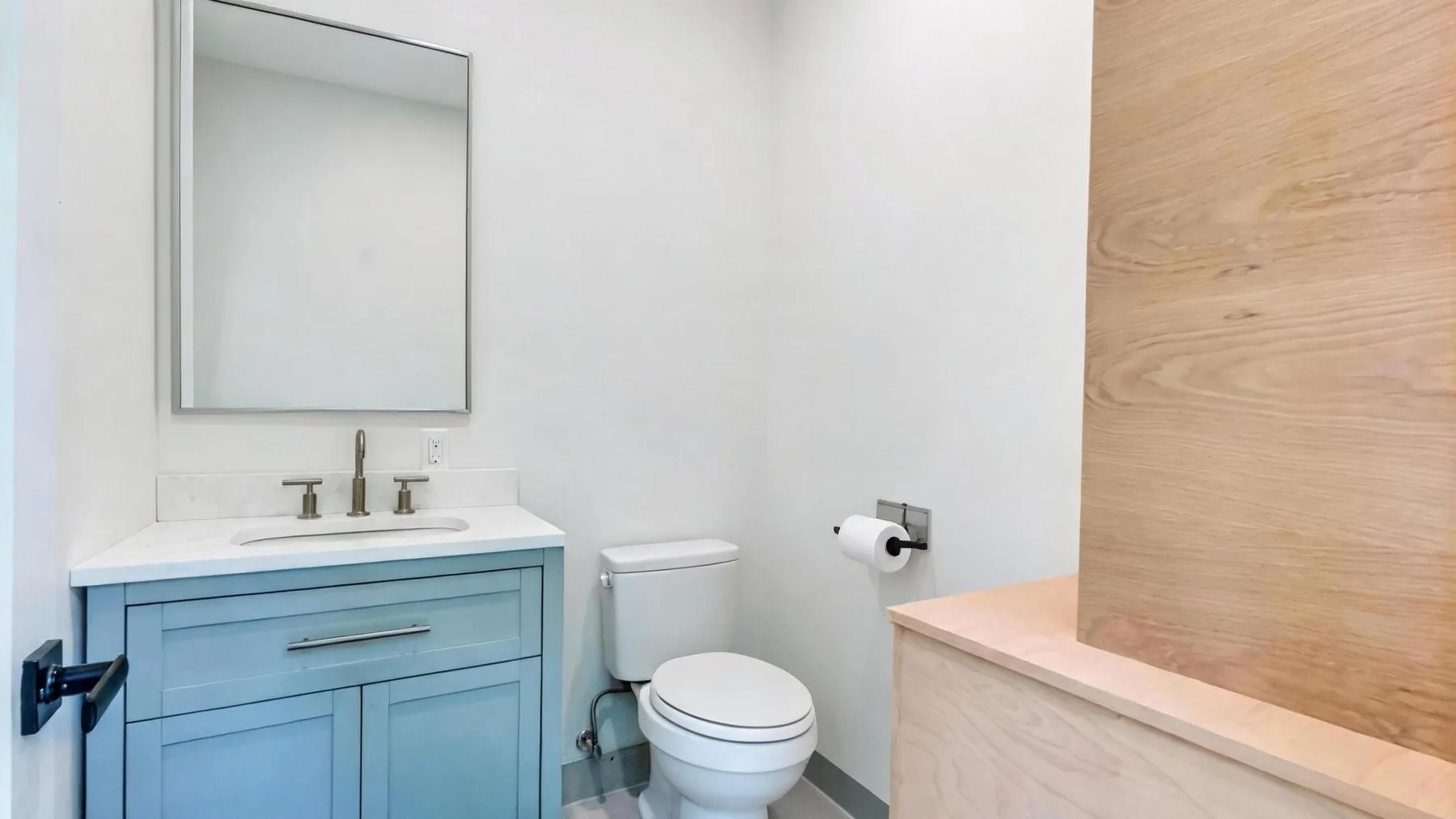 A bathroom with a sink, mirror, and toilet beside a wood-paneled partition.