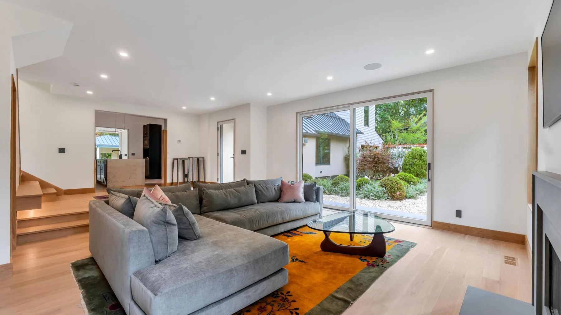 A bright living room with sectional seating and glass doors opening to a garden.