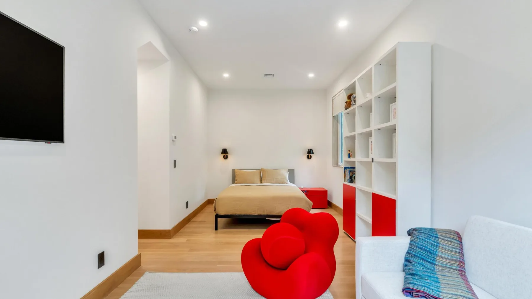 A bright bedroom with a bed, open shelving, and colorful seating.
