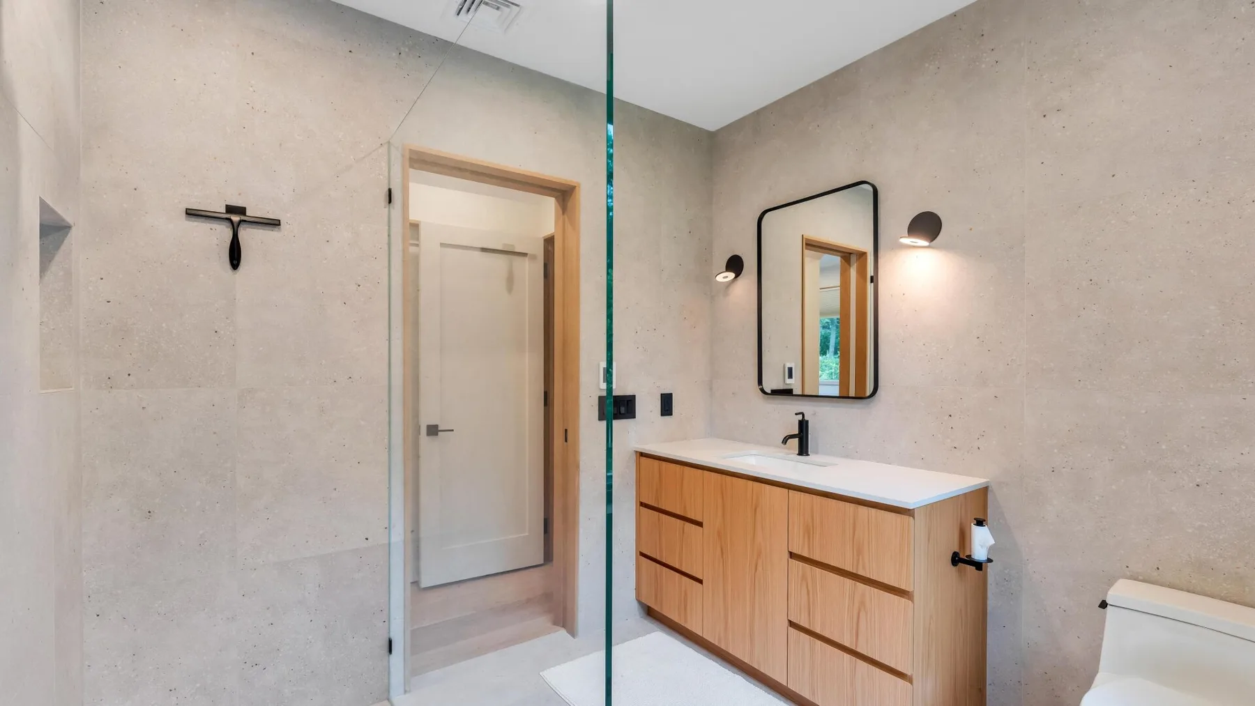 A bathroom with a wood vanity, mirror, and glass shower partition.