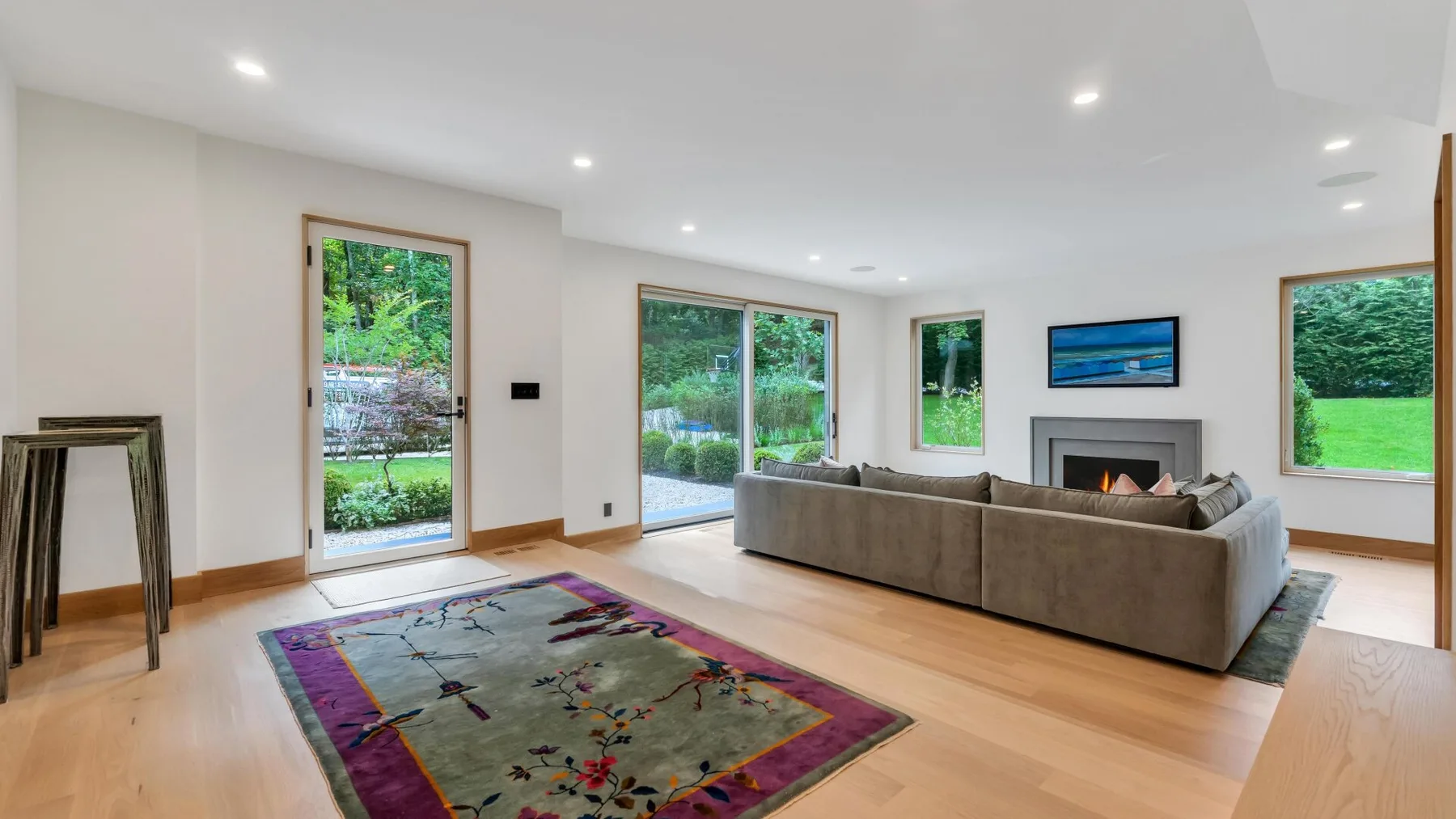 A bright living room with a large area rug and seating facing a fireplace.