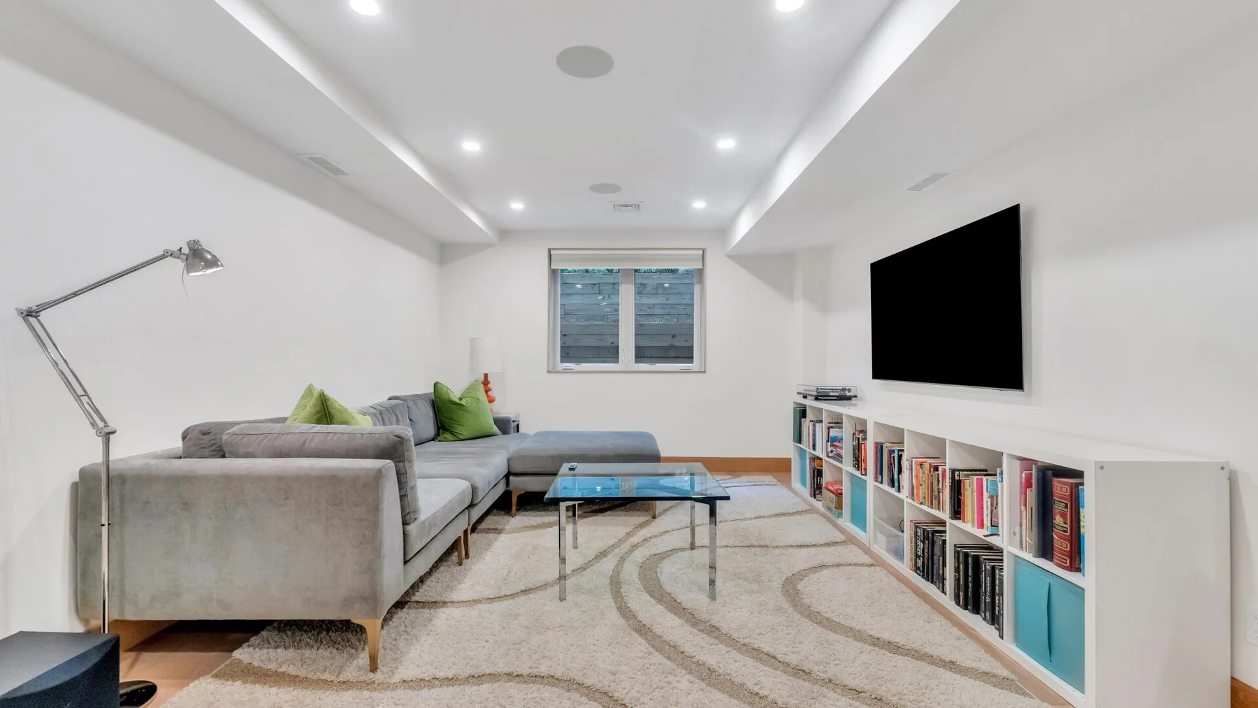 A bright living room with sectional seating, a coffee table, and a wall-mounted television.