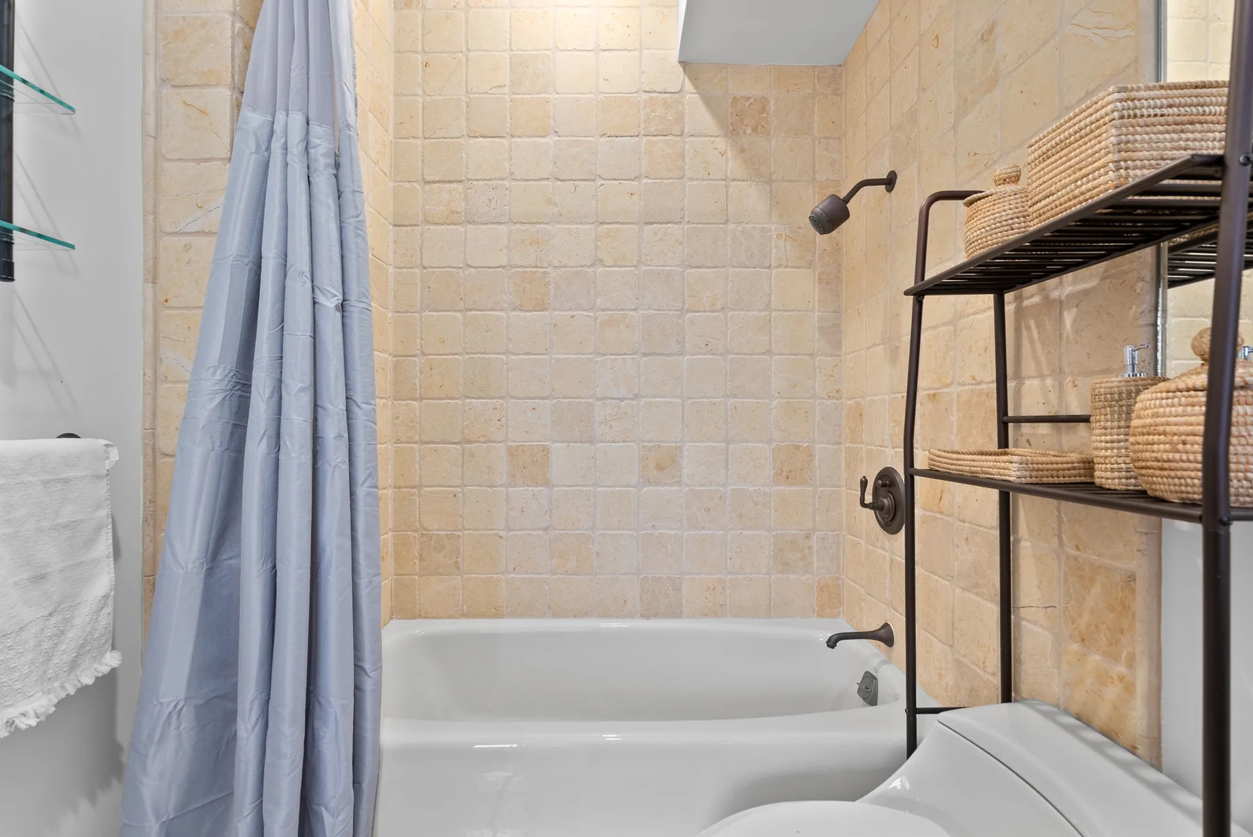 Un baño alicatado con bañera, cortina de ducha y estantes de almacenamiento.