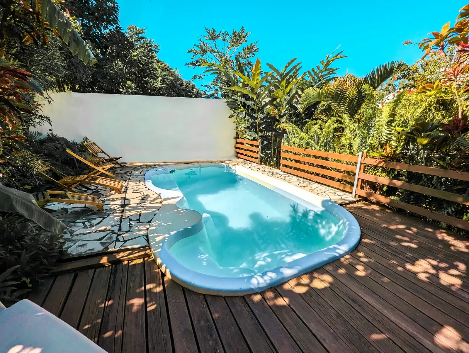 La piscina de Coco Vanille, la terraza de madera y las tumbonas en el jardín tropical
