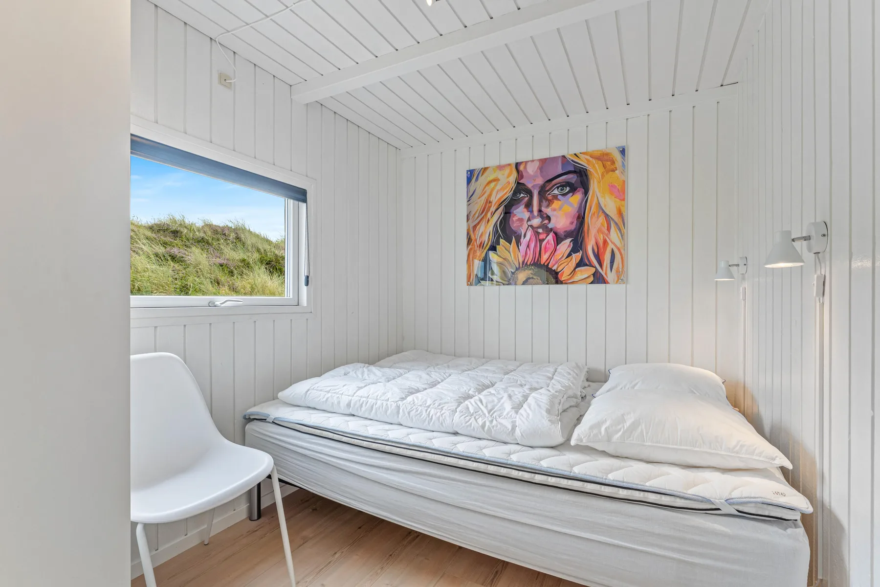 Un dormitorio luminoso con una cama bajo un retrato colorido.