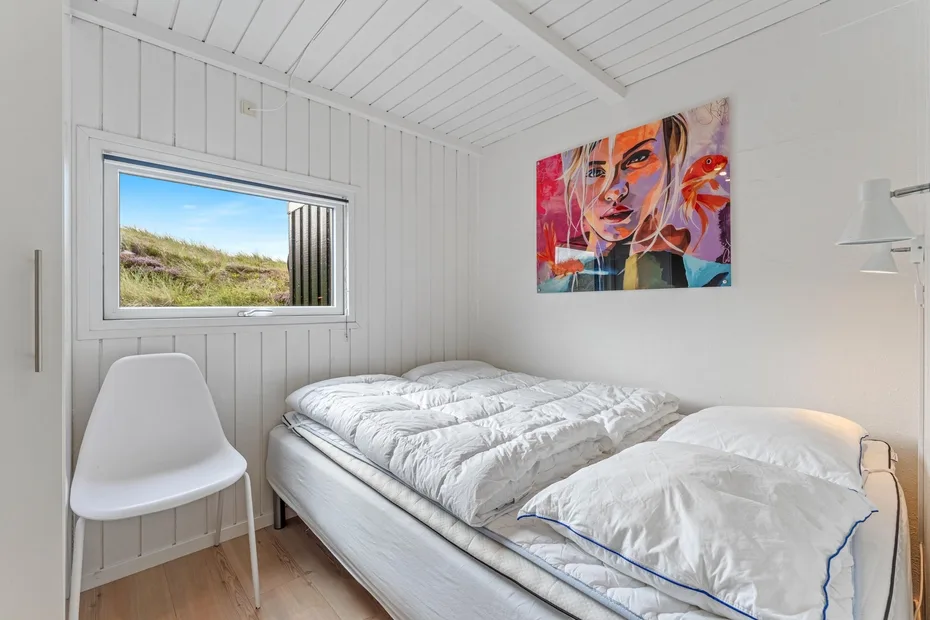 Un dormitorio luminoso con una cama blanca bajo un colorido retrato artístico.