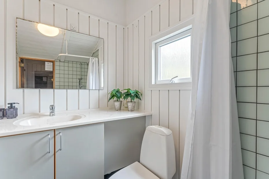 Un baño luminoso con un tocador largo, una ventana y una cortina de ducha.
