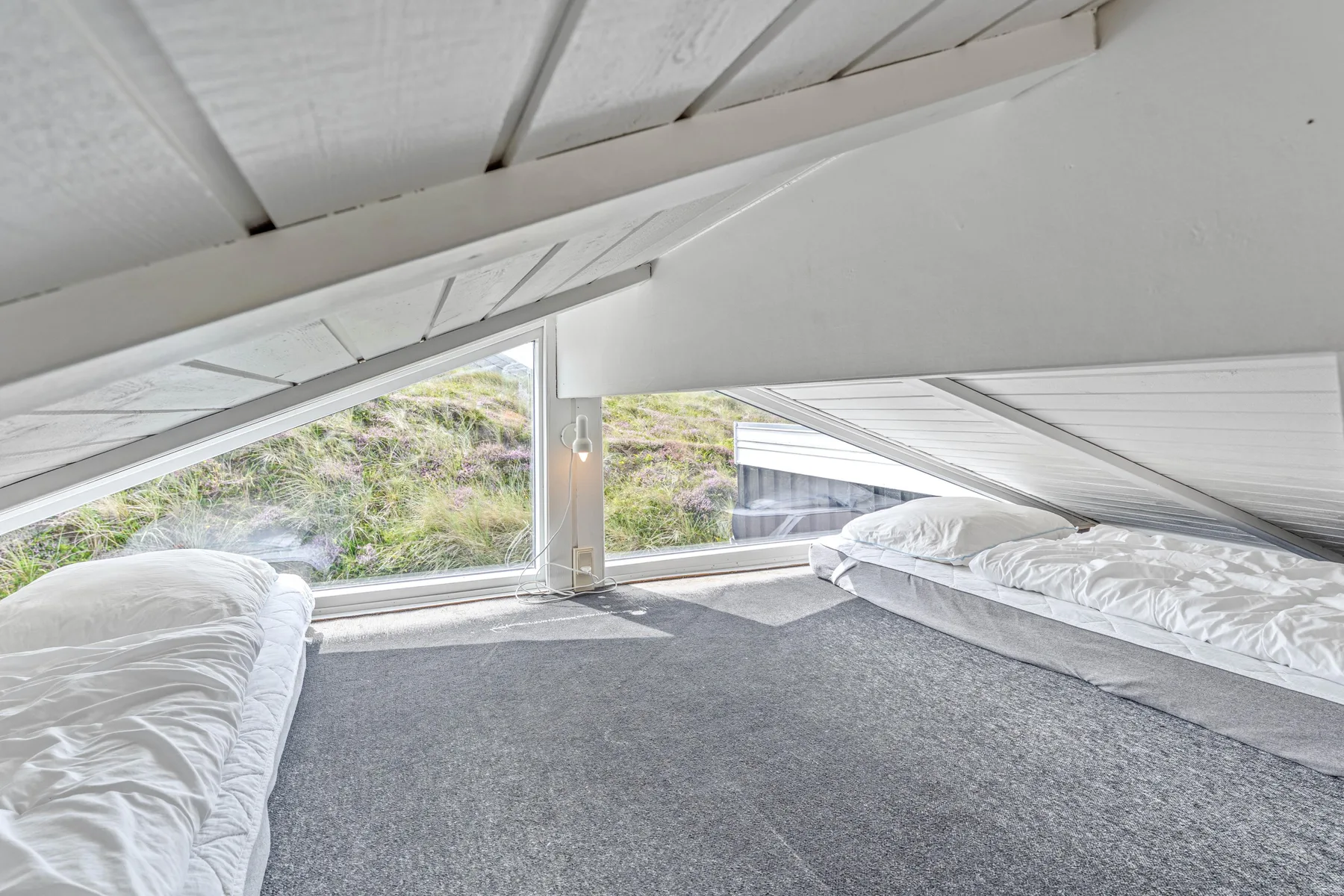 Un espacio para dormir de techo bajo, con ropa de cama a ambos lados y ventanas inclinadas.