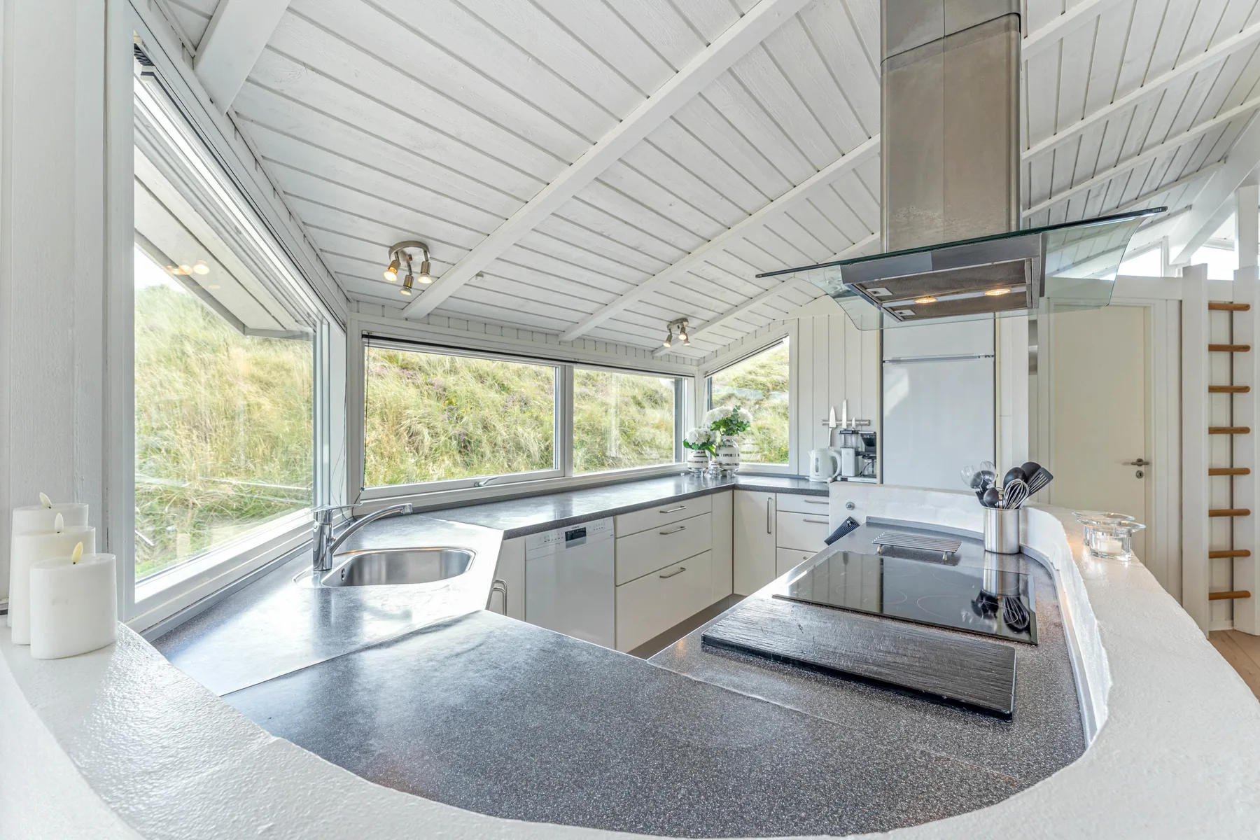 Una cocina luminosa con encimera curva, placa de cocción y grandes ventanales.