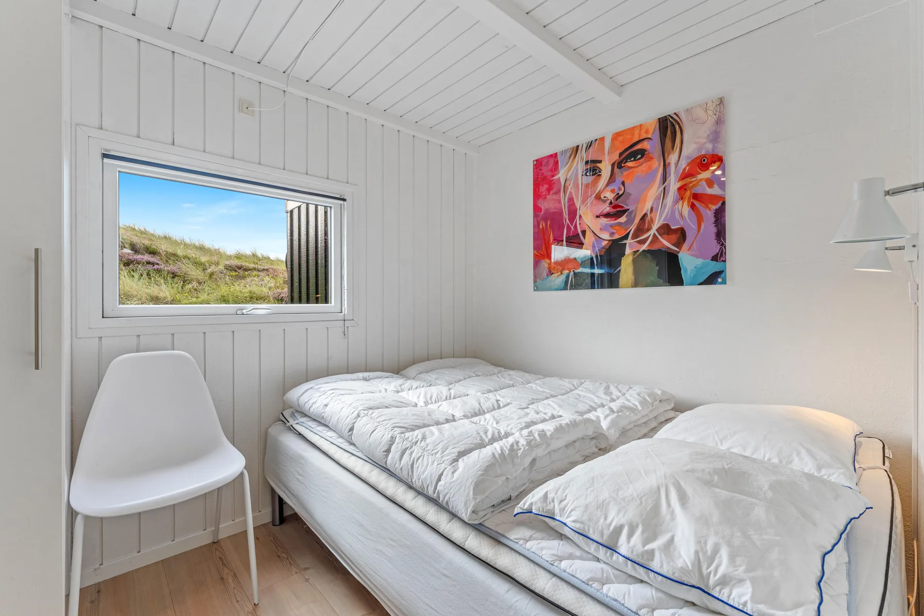 Un dormitorio luminoso con una cama, una ventana y una obra colorida en la pared.