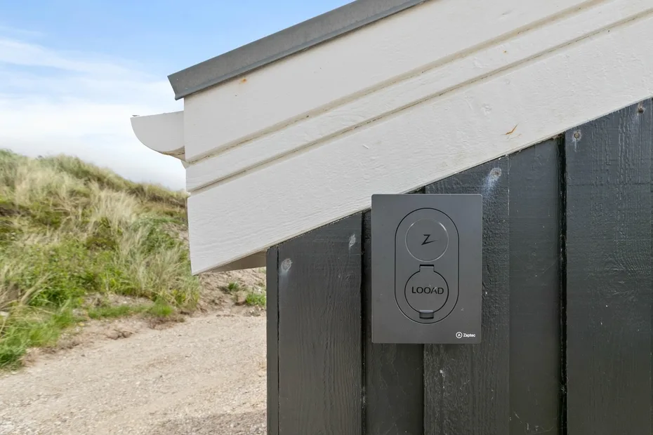 Un panel oscuro al aire libre junto a un camino de arena y dunas cubiertas de hierba.