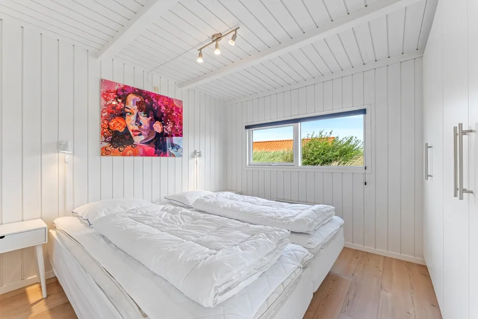 Un dormitorio blanco y luminoso con una cama grande bajo un cuadro colorido.