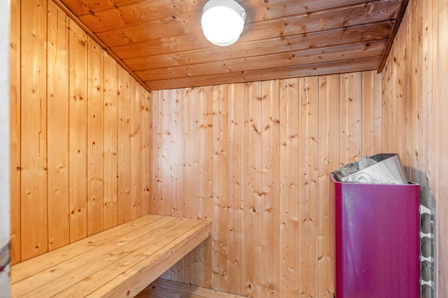 Una sauna revestida de madera con un banco y un calentador cubierto.