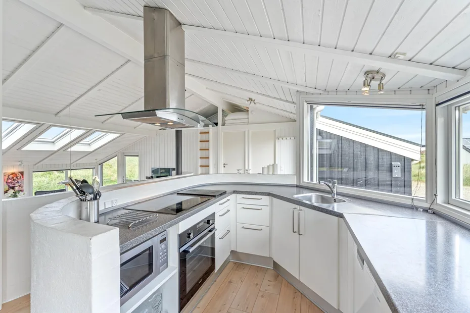 Una cocina luminosa con gabinetes blancos, amplias encimeras y ventanas grandes.