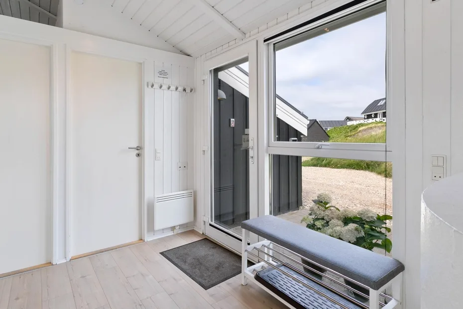 Una entrada luminosa con un banco junto a grandes ventanas con vistas al exterior.