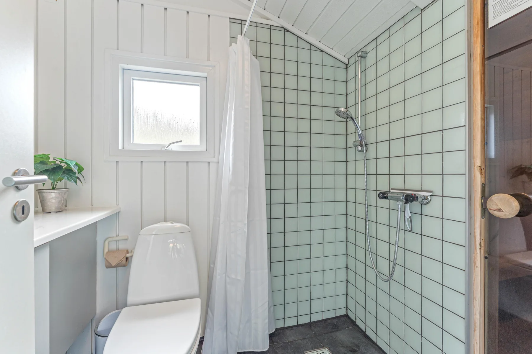 Un baño luminoso con un inodoro junto a una ducha alicatada.