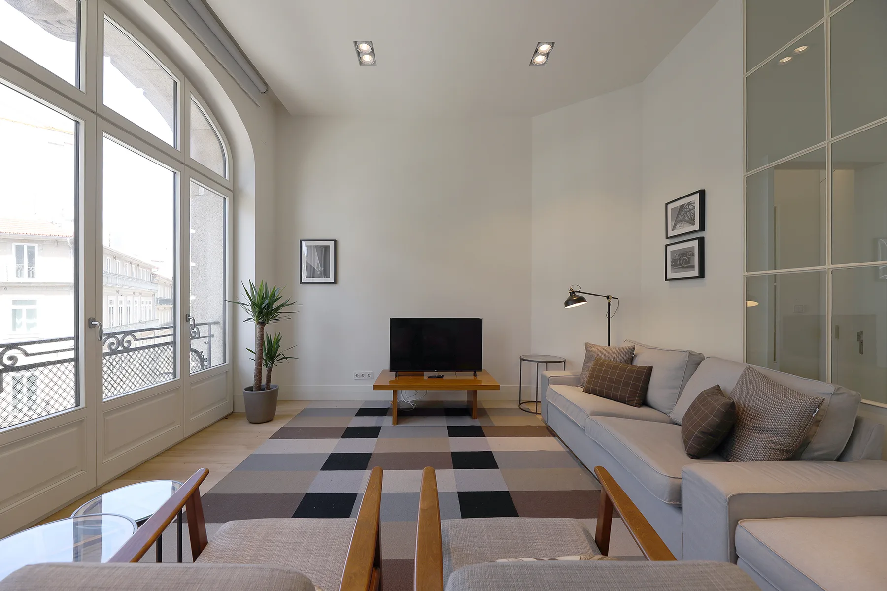 Bright living room with seating, a television, and tall arched windows.