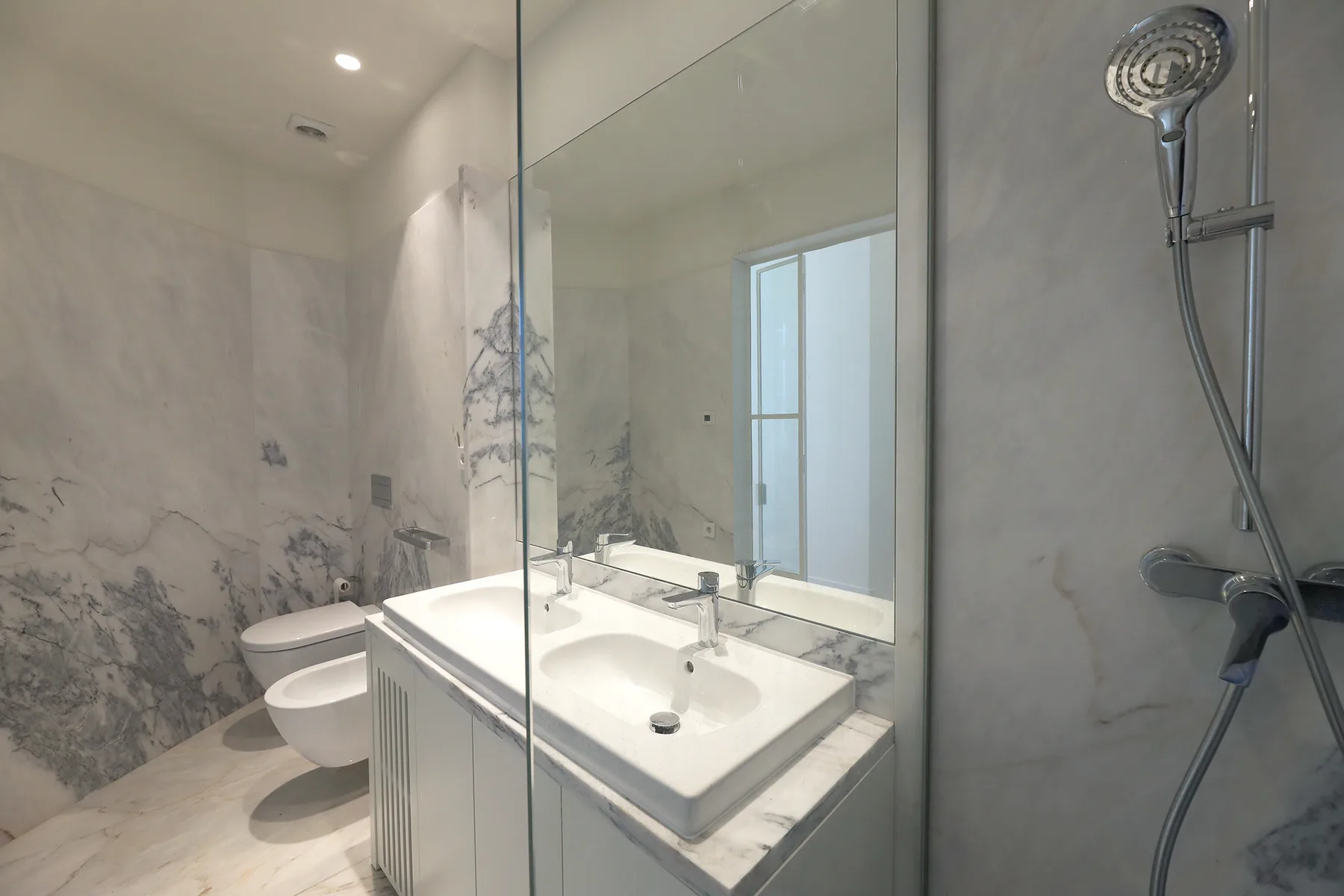 Un baño de mármol con lavabo, inodoro y ducha de vidrio.