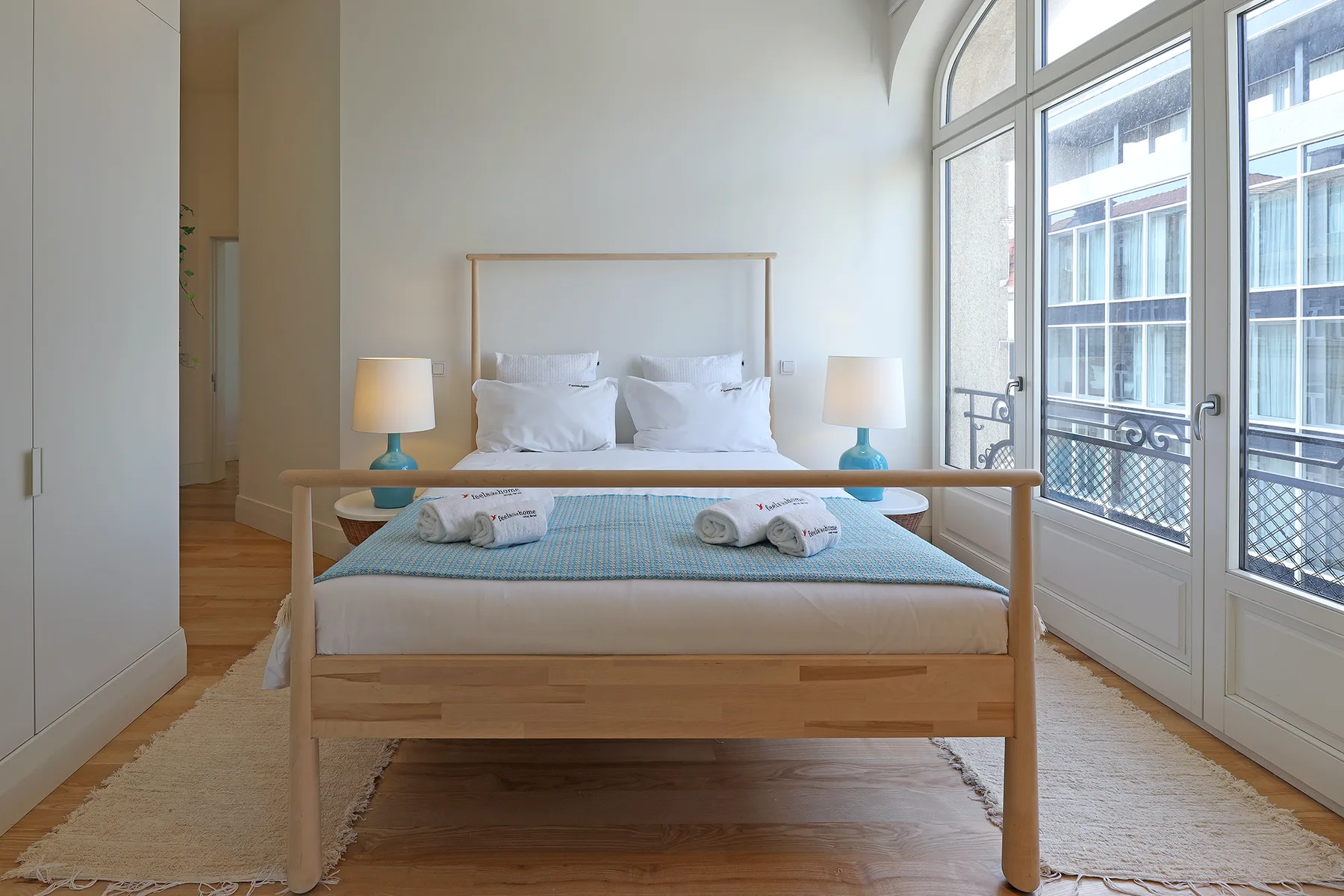 A bright bedroom with a neatly made bed beside tall windows.