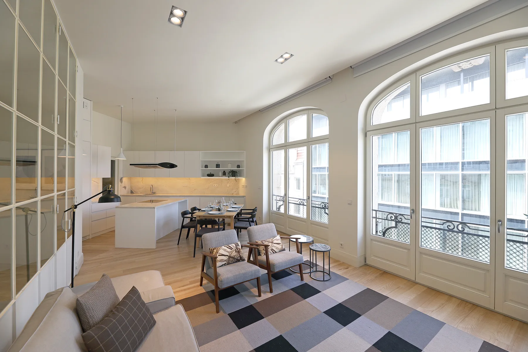 Una luminosa sala de estar y comedor con grandes ventanas arqueadas y cocina abierta.