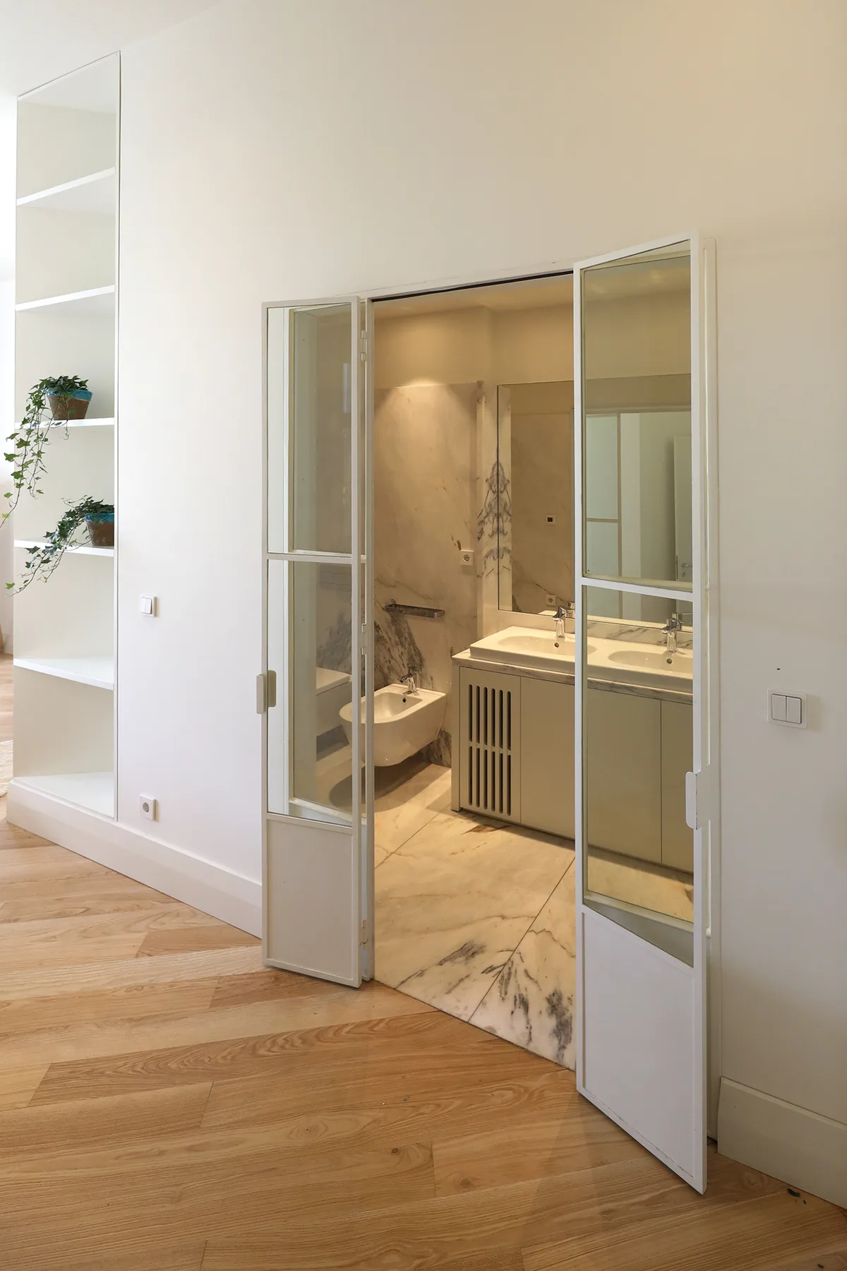 Se ve un baño con lavabo e inodoro a través de puertas abiertas con paneles de vidrio.