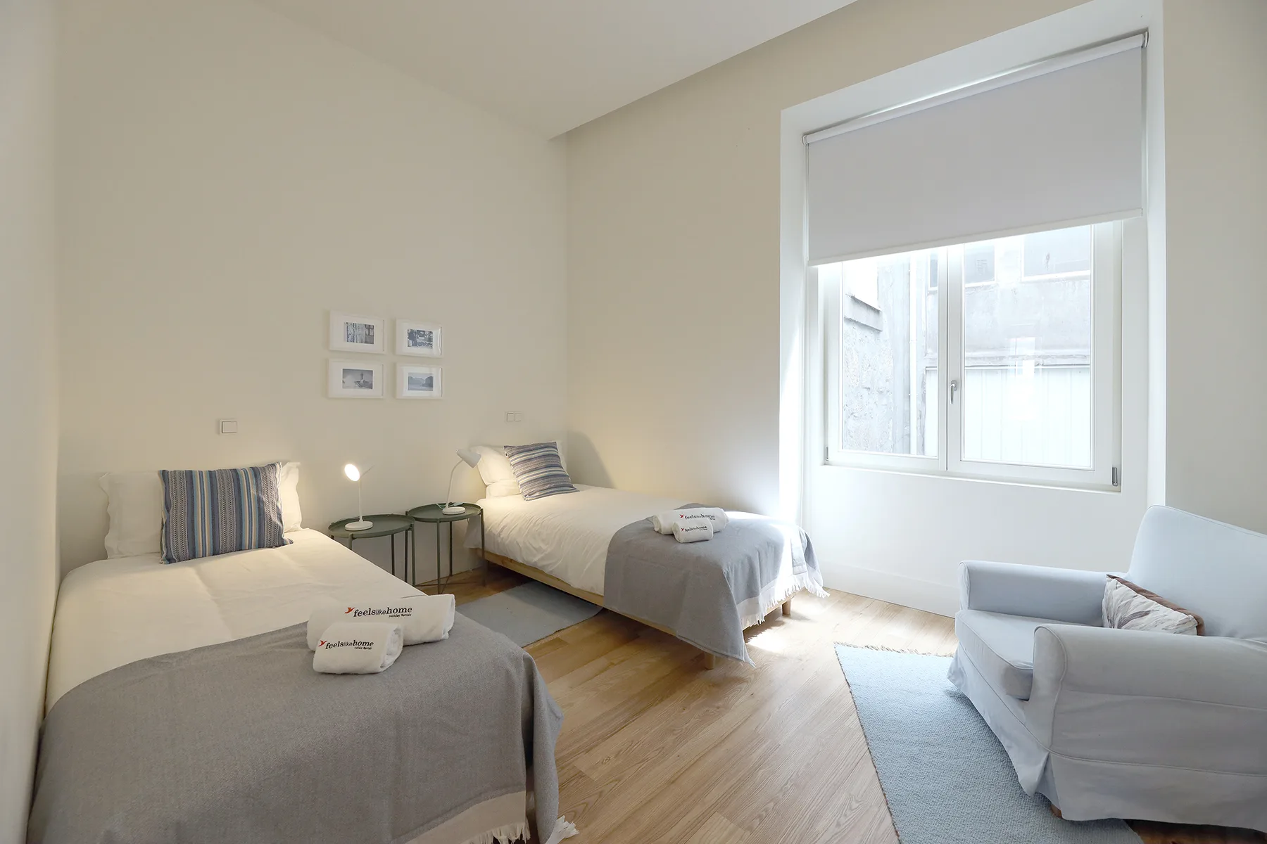 Un dormitorio luminoso con dos camas y una ventana con vistas a edificios cercanos.