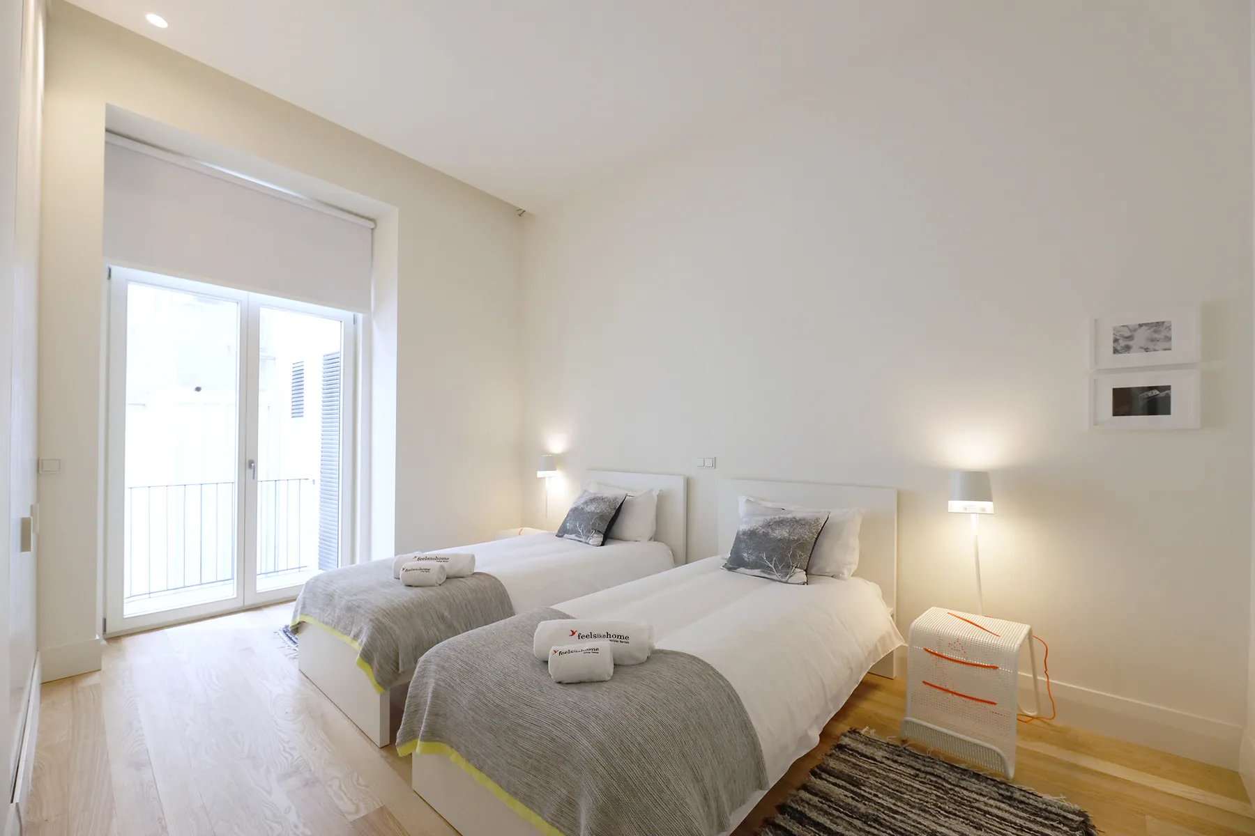 A bright bedroom with two beds, bedside lamps, and a large window.