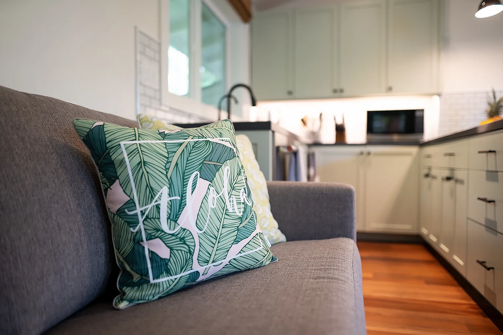 Un sofá gris con cojines estampados está junto a una cocina luminosa.