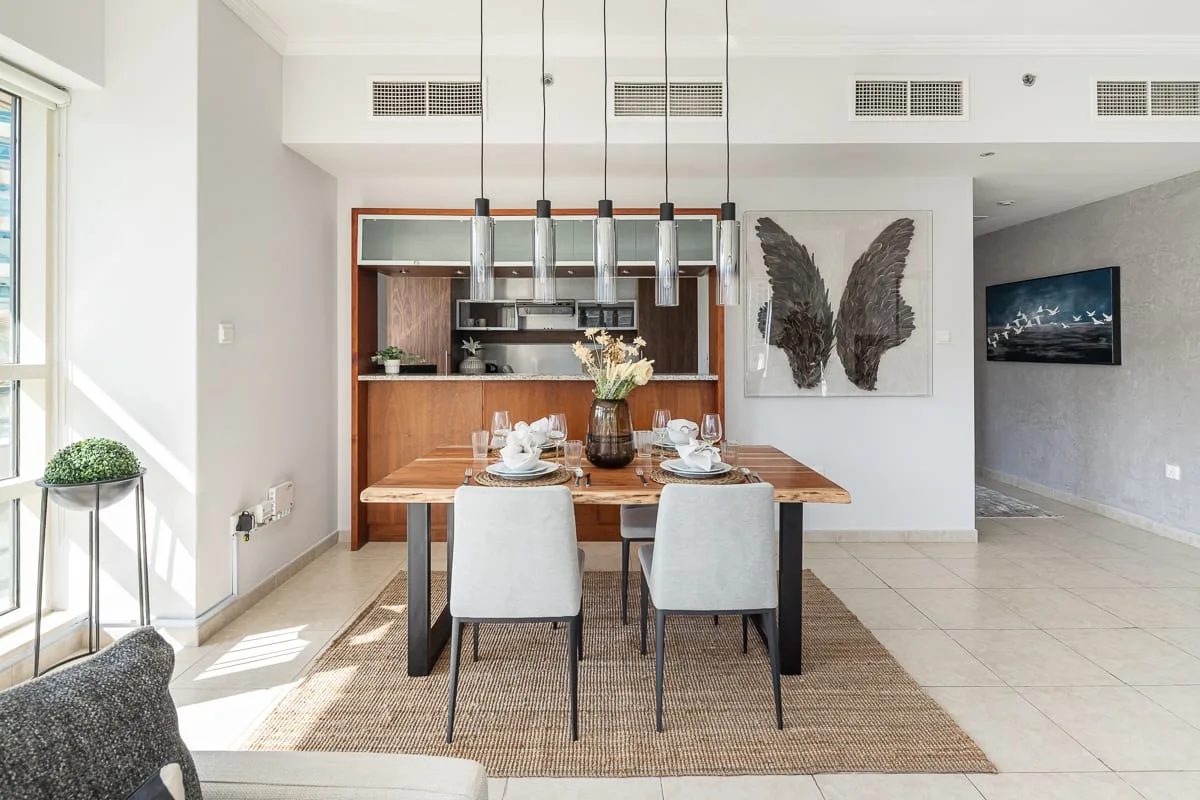 Comedor con la mesa puesta, lámparas colgantes y ventanas grandes.