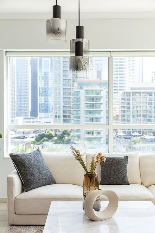 Una sala luminosa con un sofá frente a grandes ventanas con vista a edificios de la ciudad.