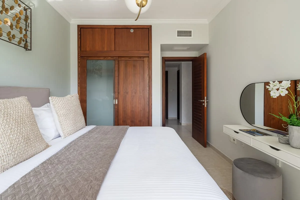 Un dormitorio con una cama bien tendida, un armario de madera y un tocador.