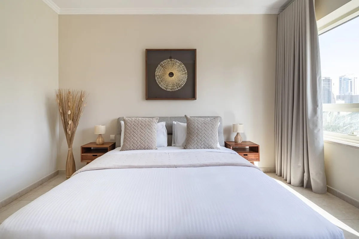 Un dormitorio luminoso con una cama bien tendida y un cuadro sobre el cabecero.