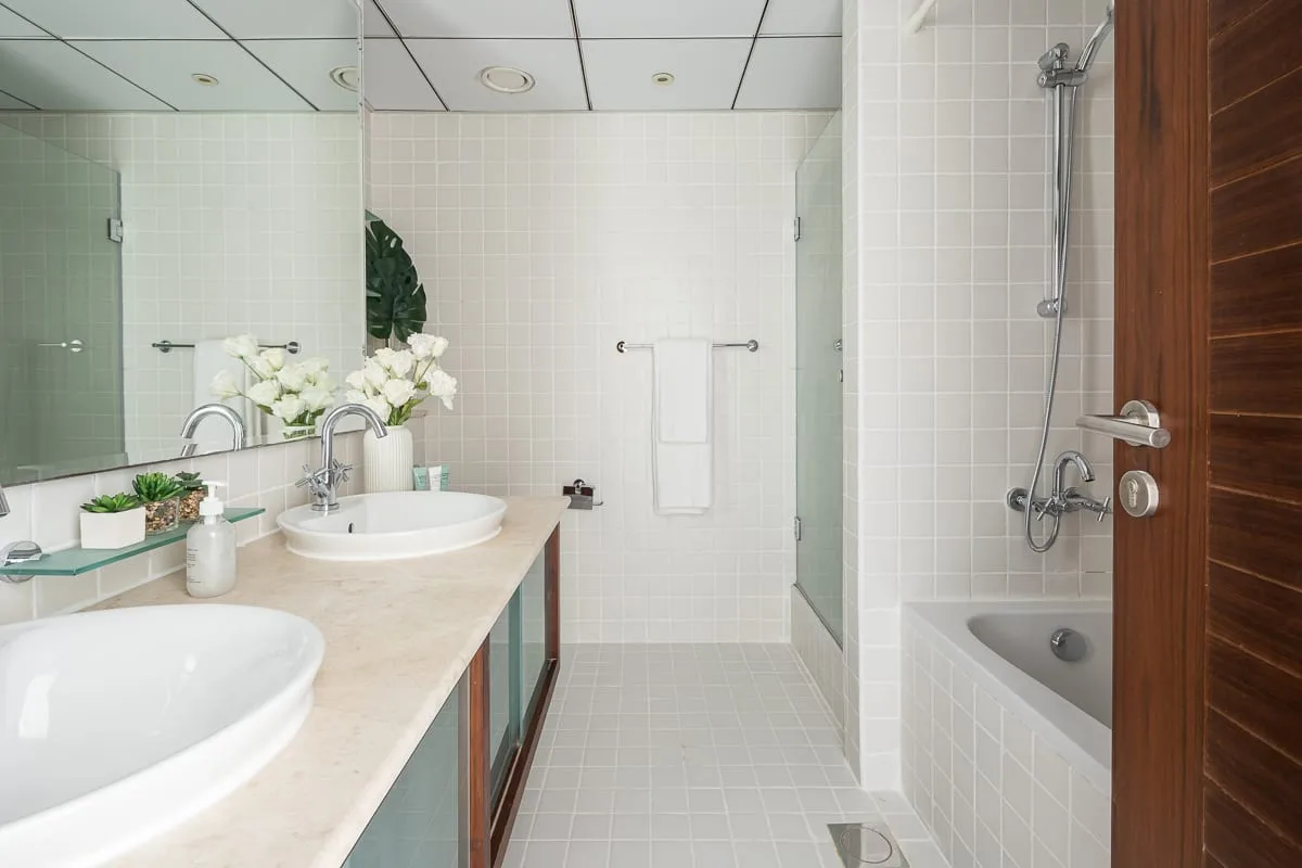 Un baño de azulejos con lavabos junto a la encimera y una bañera al lado de la ducha.