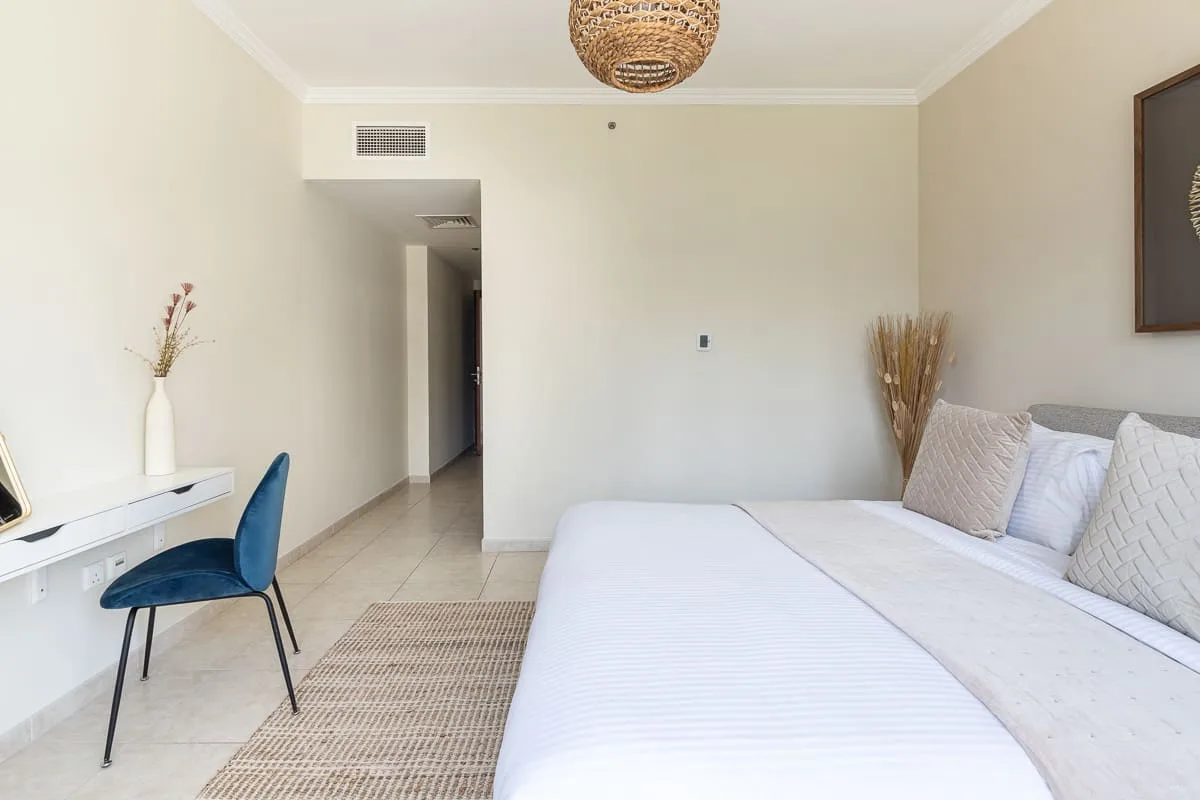 Un dormitorio con una cama blanca, un escritorio y una lámpara tejida en el techo.