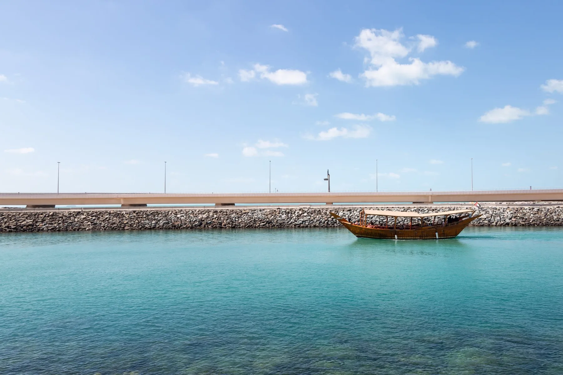 Una embarcación de madera flota en aguas turquesas junto a un rompeolas rocoso.