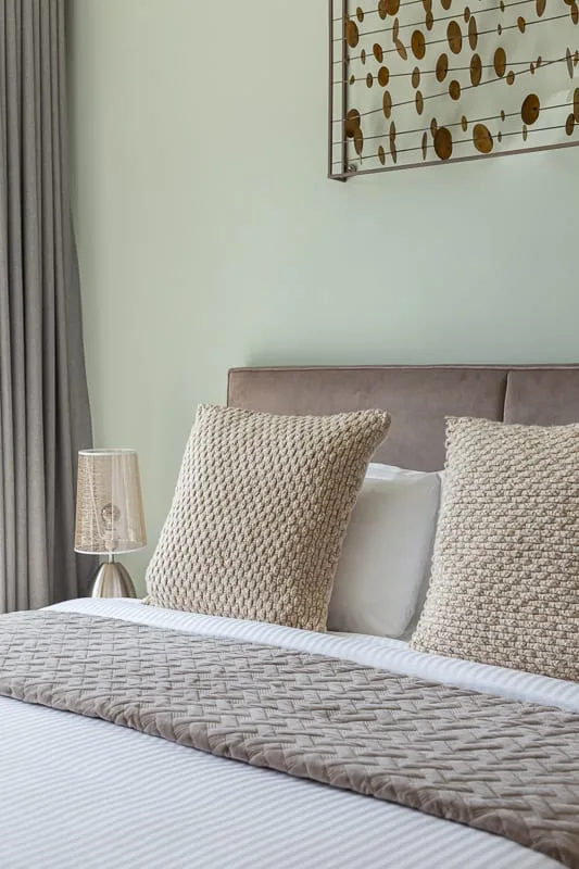 Una cama bien arreglada tiene cojines texturizados y un cabecero tapizado gris.
