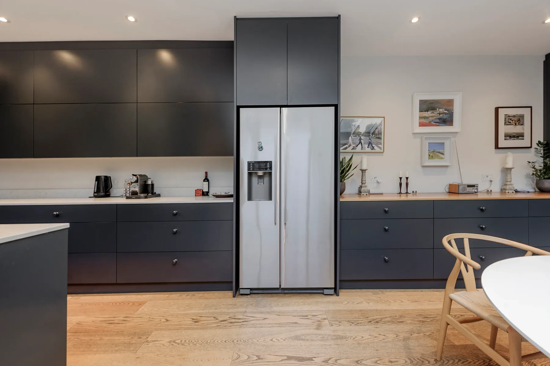 A modern kitchen with dark cabinets, a refrigerator, and a dining table.