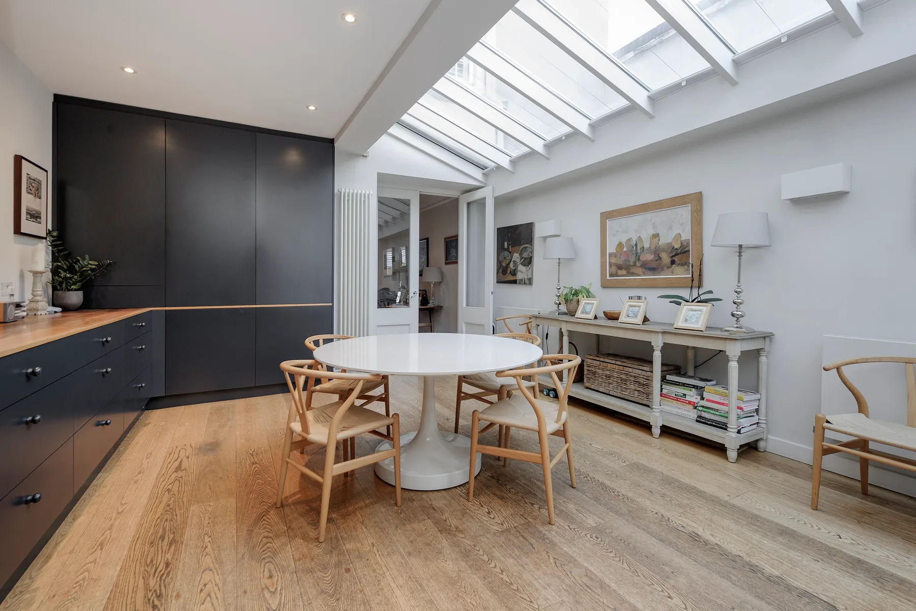 A dining area with a round table and chairs beneath a large skylight.