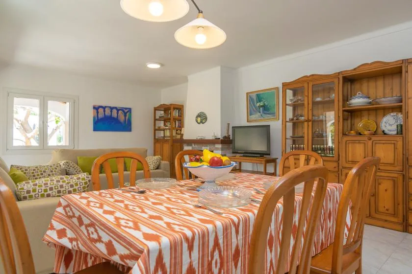 A dining area with a patterned tablecloth and wooden chairs, beside a living area.