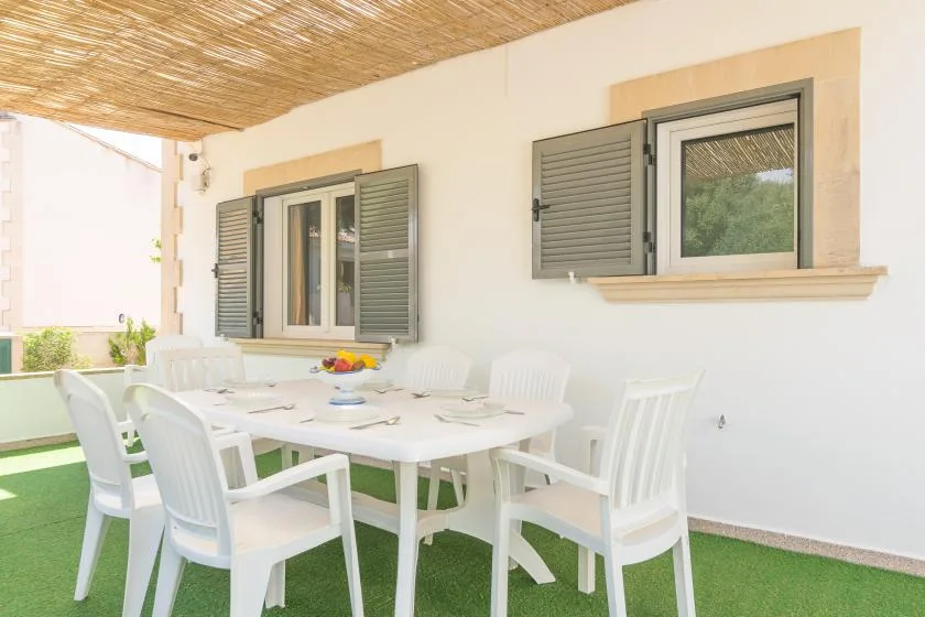 An outdoor dining area with a white table and chairs beneath a woven canopy.