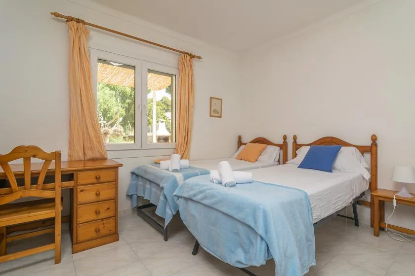 A bedroom with two beds, pale blue covers, and a window overlooking greenery.