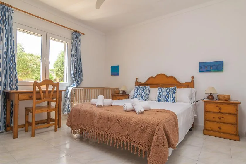 A bedroom with a double bed, blue patterned curtains, and a wooden desk.