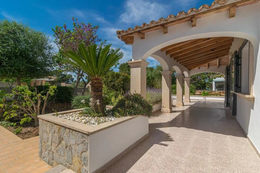 A covered patio walkway with arched openings overlooks a landscaped garden.