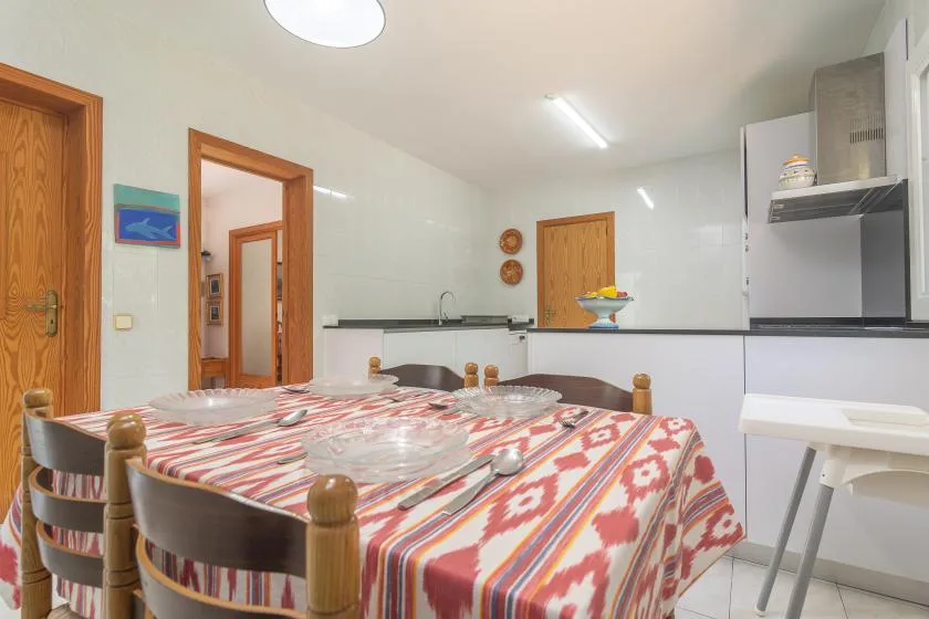 A dining area with a patterned tablecloth, beside a bright kitchen.