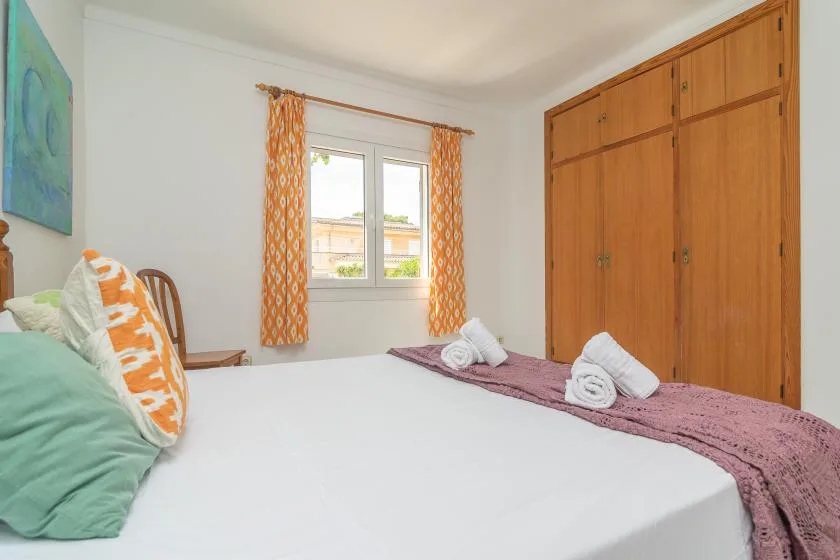 A bedroom with a bed, orange curtains, and wooden wardrobes.
