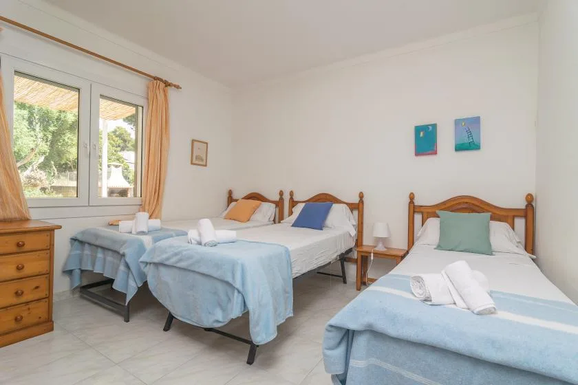 A bright bedroom with three beds dressed in pale blue bedding.