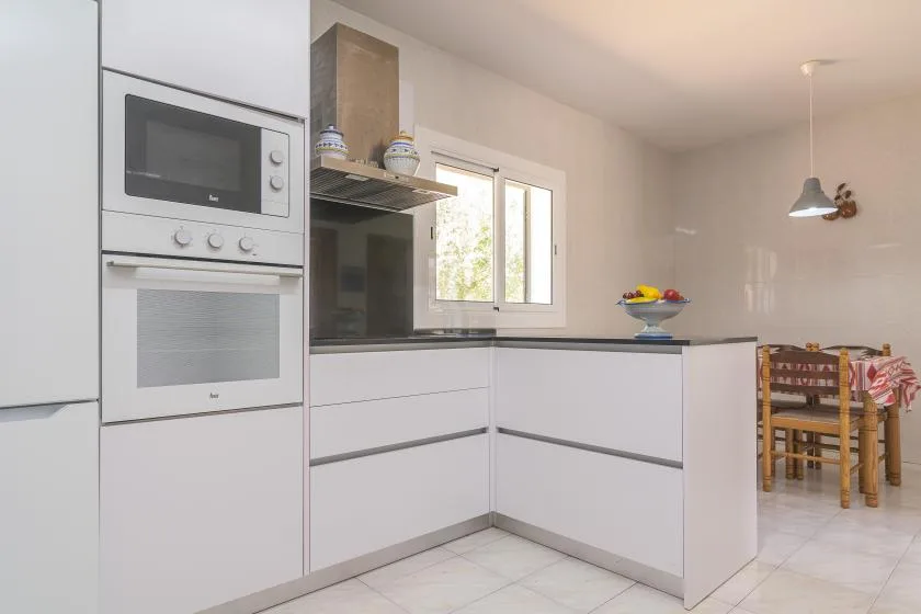 A bright kitchen with white cabinetry, built-in appliances, and a dining table.