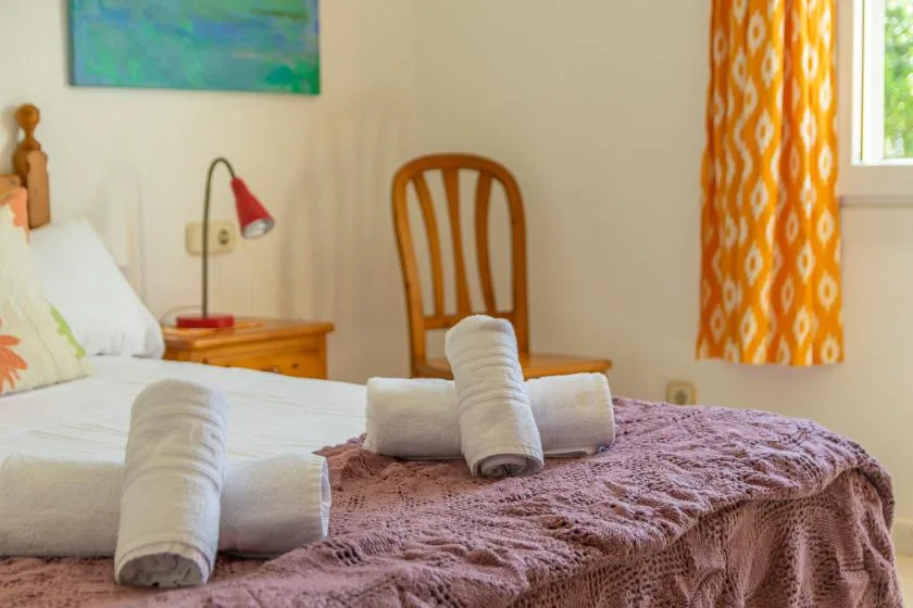 A bedroom with a bed covered by a purple blanket and rolled towels.
