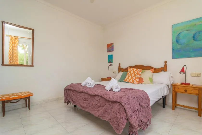 A bedroom with a bed dressed in white linens and a mauve coverlet.
